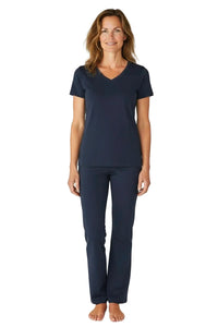 Woman wearing navy blue scrub top and pants standing barefoot on white background