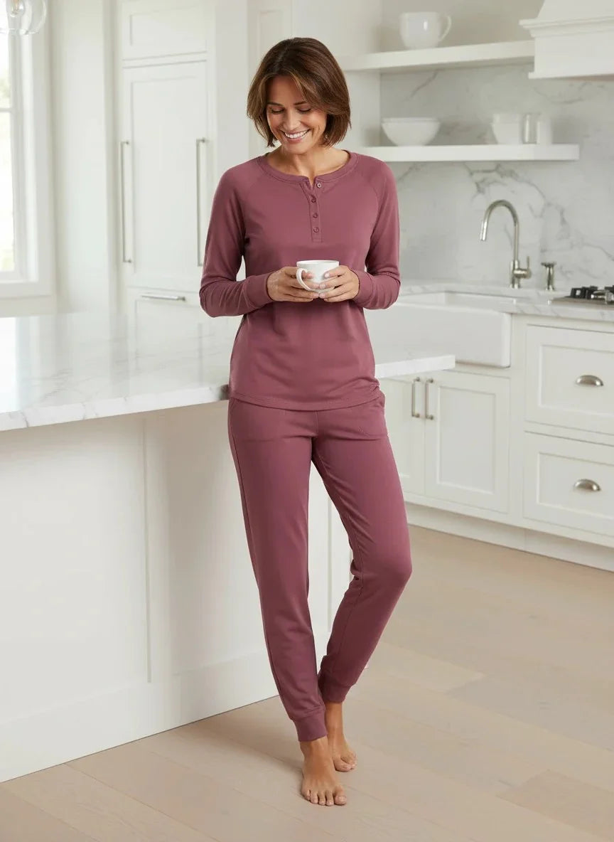 Woman in rosewood pajamas holding a white mug in a modern white kitchen